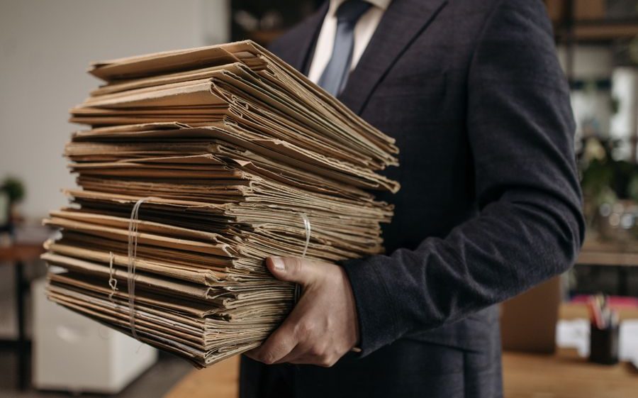 Manos de un hombre de traje sosteniendo una pila alta de carpetas de documentos